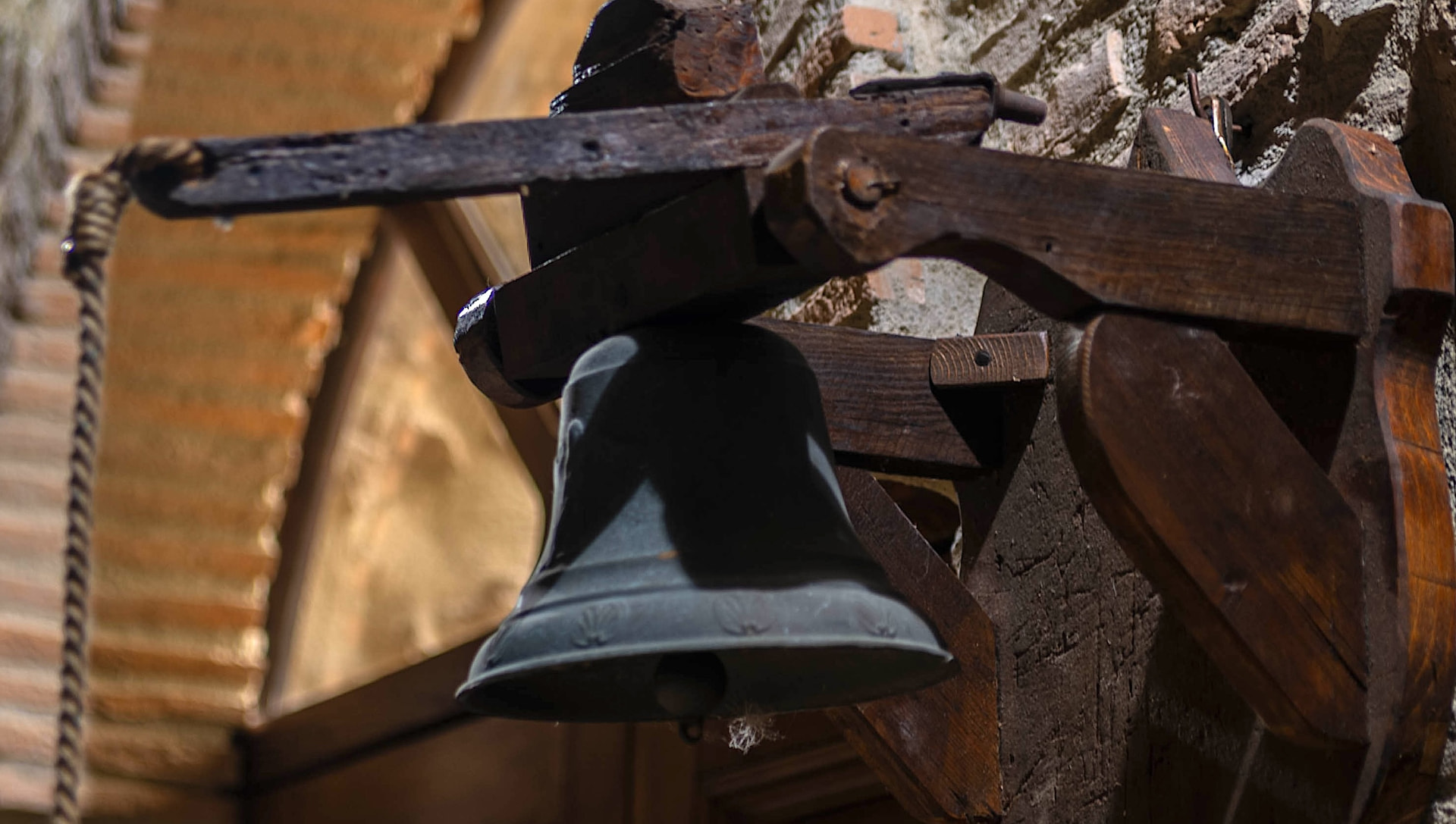 The old bell at the farmhouse entrance, hanging from its wooden yoke against the stone wall