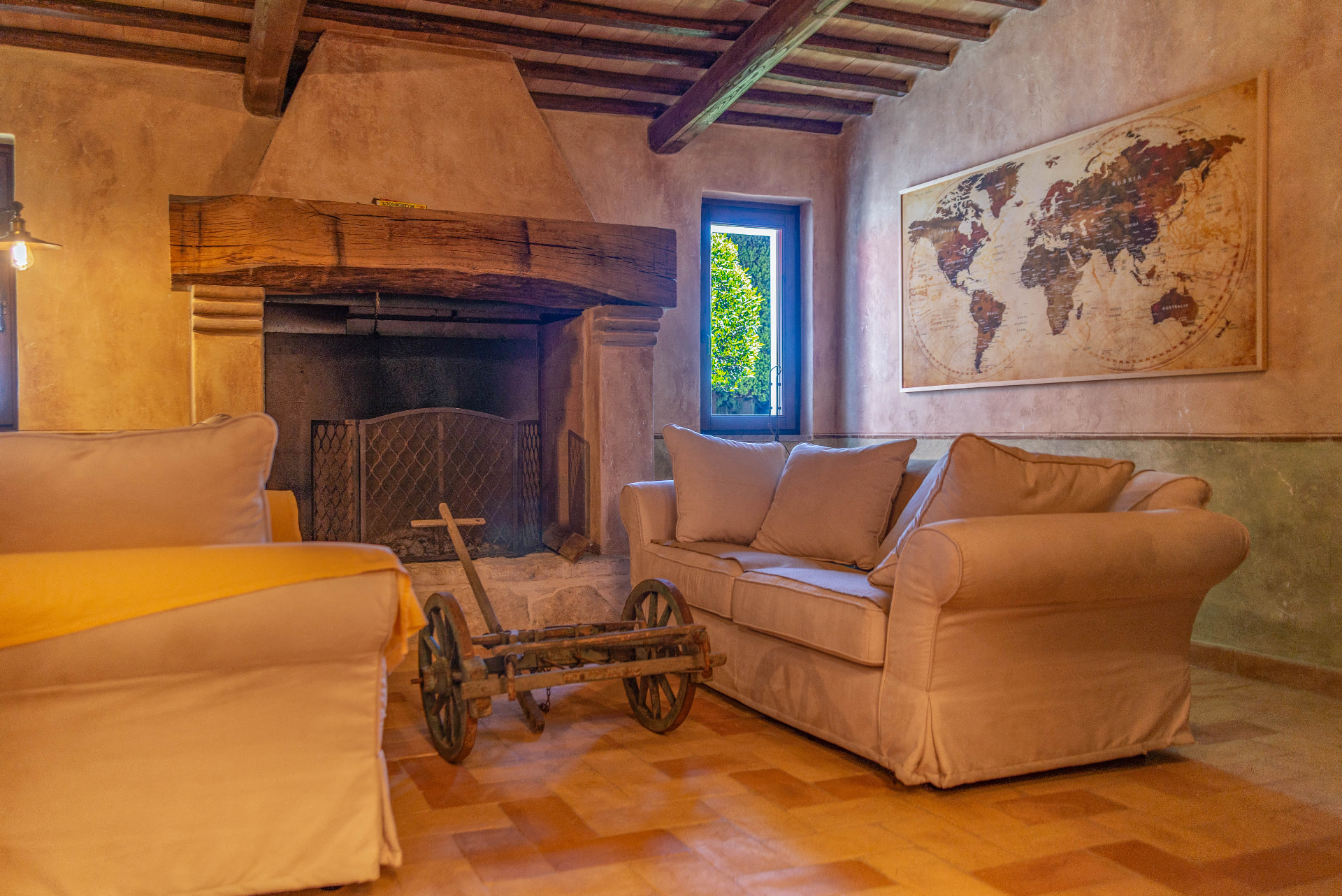The lounge around the fire: the massive oak beam, the two couches and the old milk cart coffee table, with the world map above