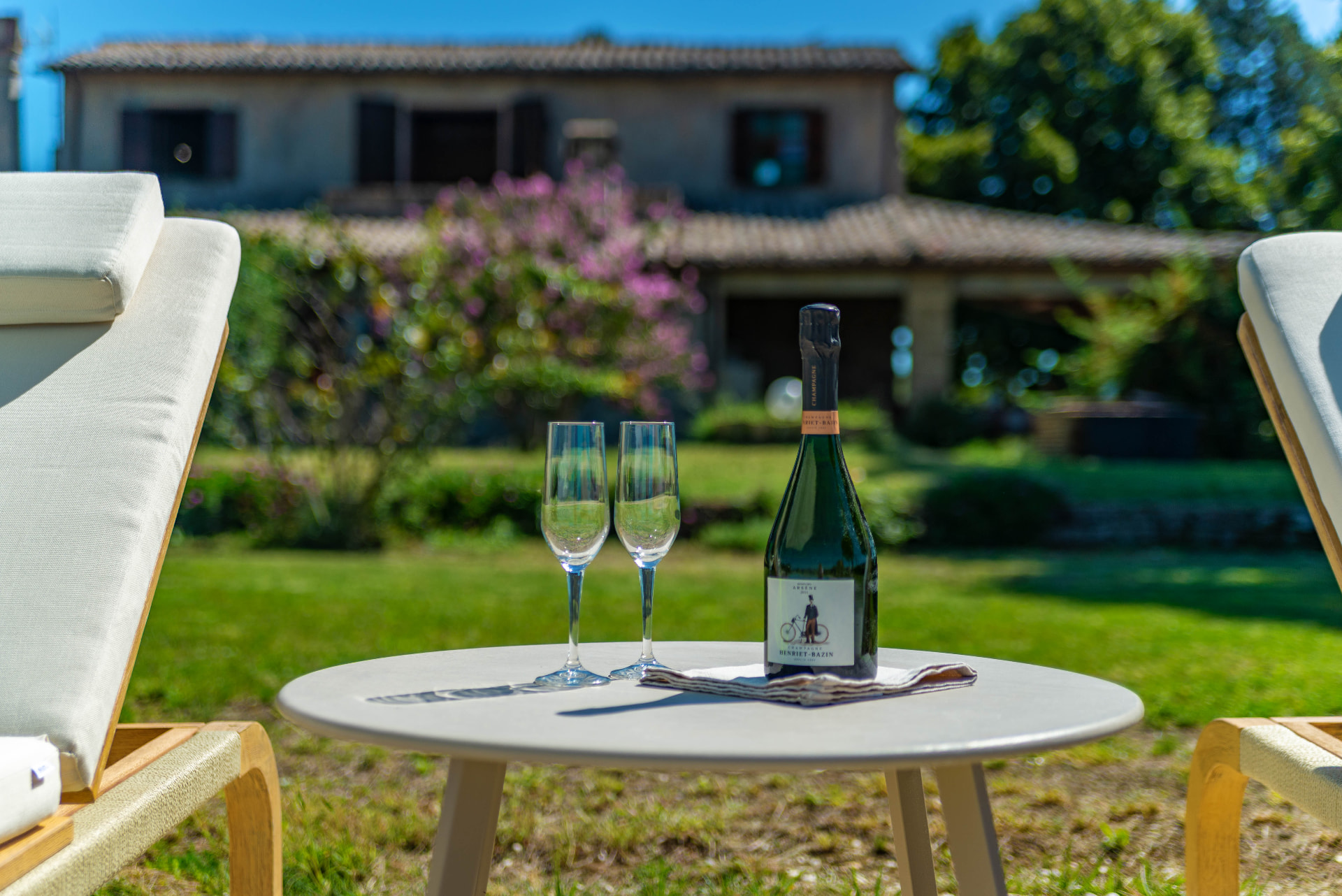 A bottle of champagne and two flutes on a small table, the house behind