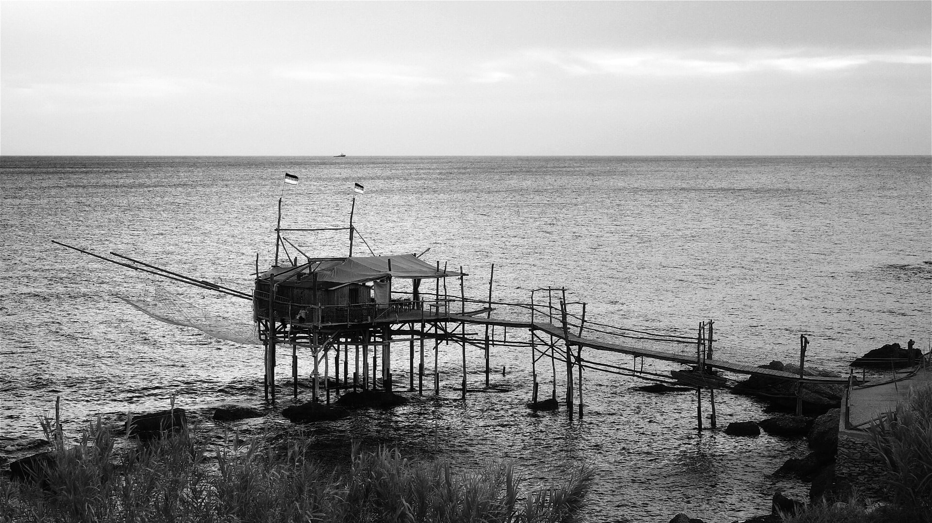 A trabocco seen in black and white, its long arms reaching over the sea