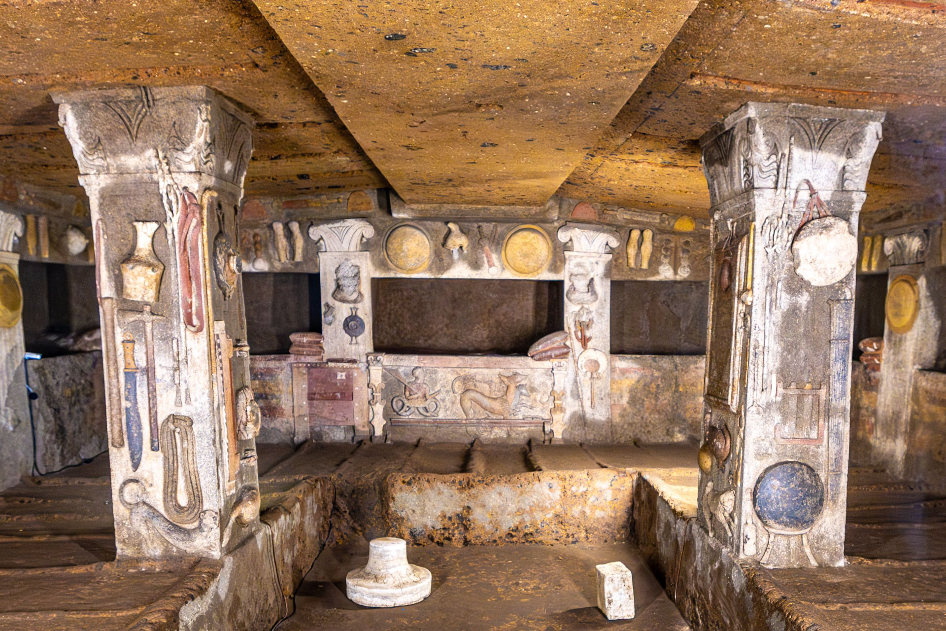 An Etruscan tomb chamber carved in tufa, its pillars covered in painted reliefs of tools, weapons and household objects