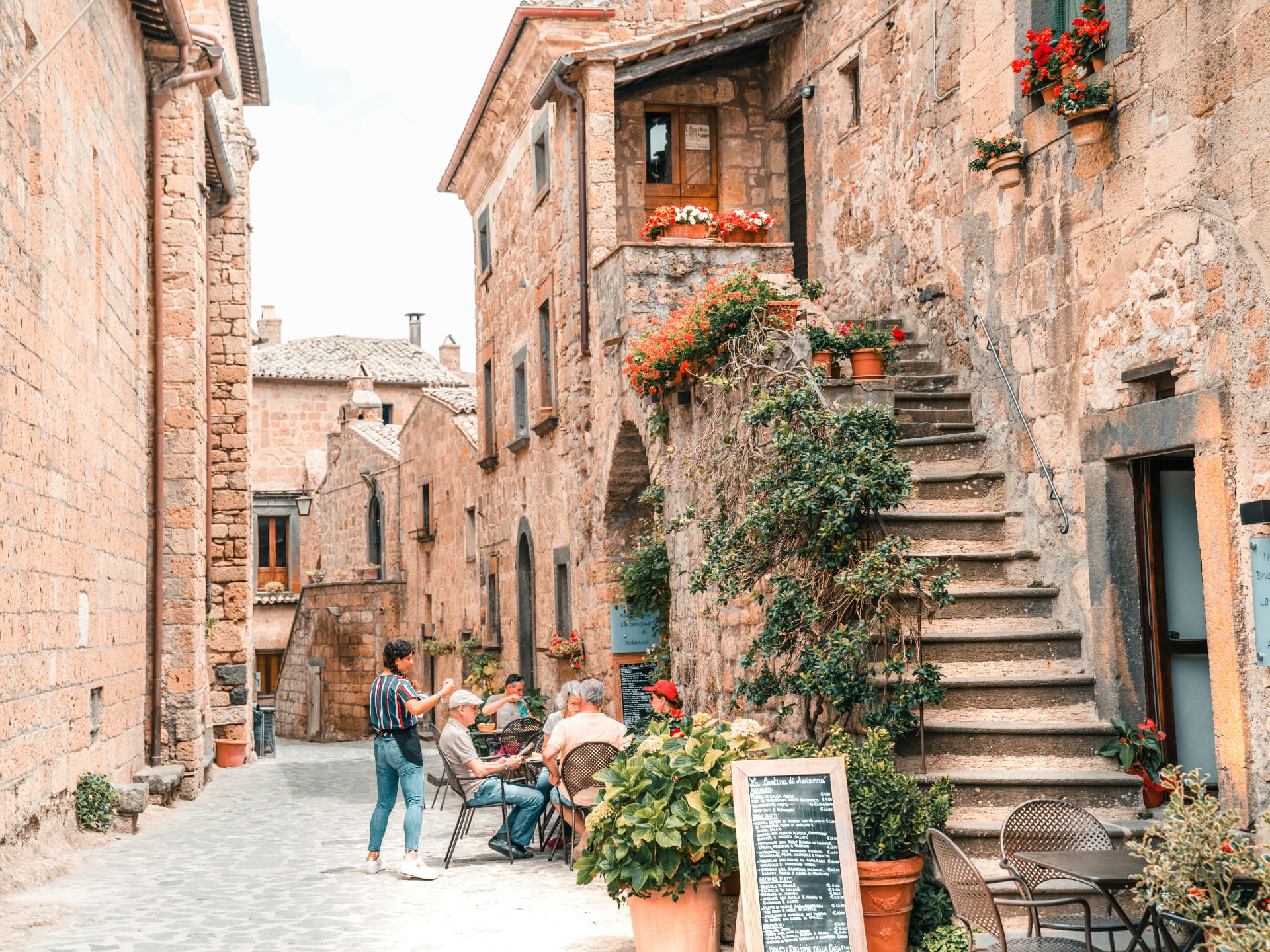 Tables set outside a trattoria down a stone alley in Civita, red geraniums on the steps
