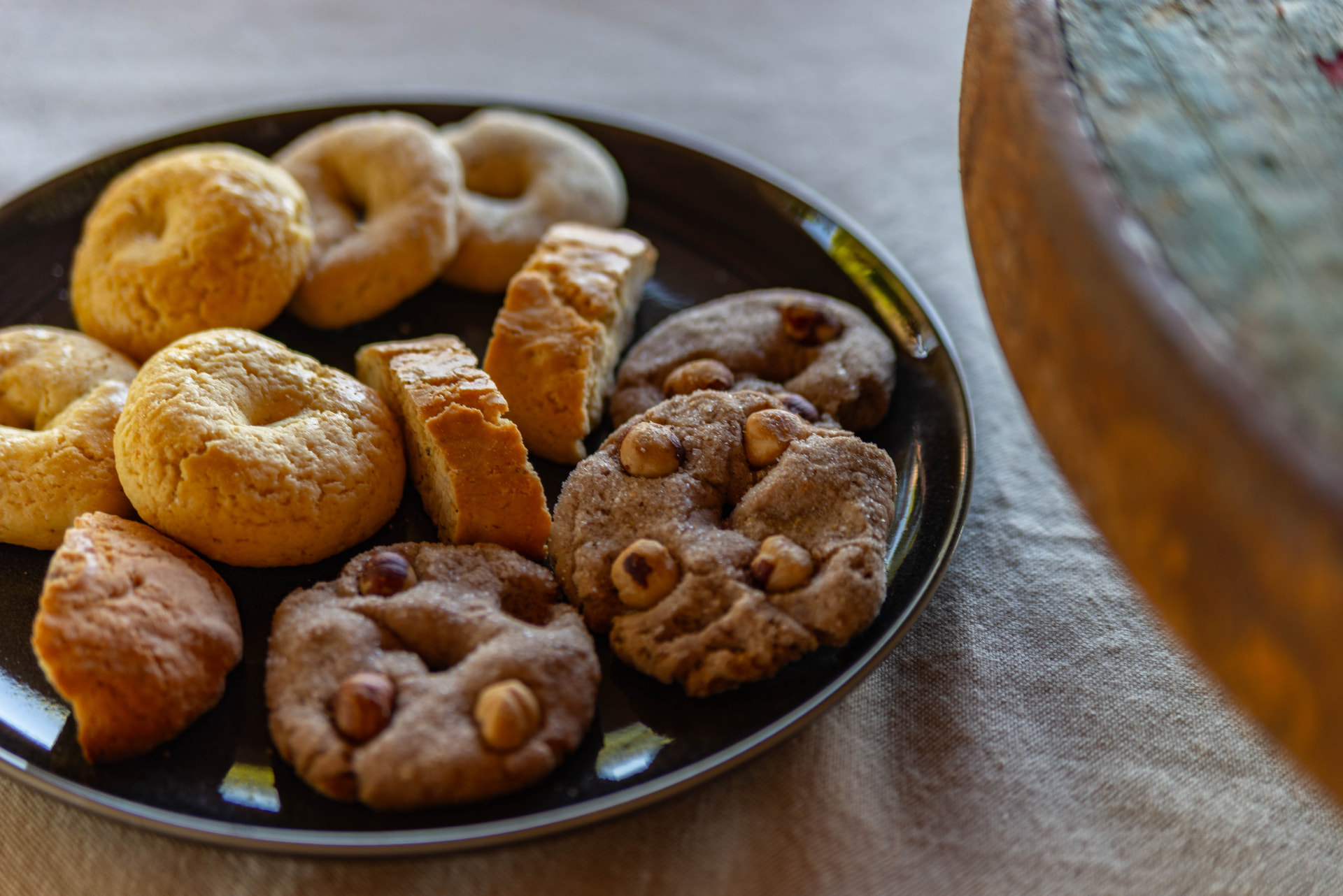 A dark plate of homemade biscuits — ciambelle, cantucci and hazelnut cookies — on the table