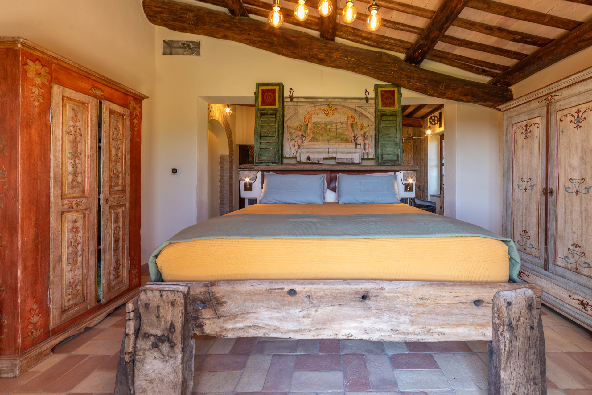 Ulivo bedroom with the bed built from ancient feeding troughs, the antique painted panel above and two painted wardrobes