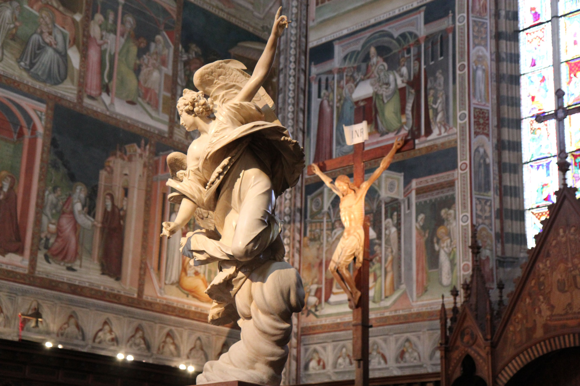 A marble angel on a carved cloud and a wooden crucifix inside Orvieto cathedral