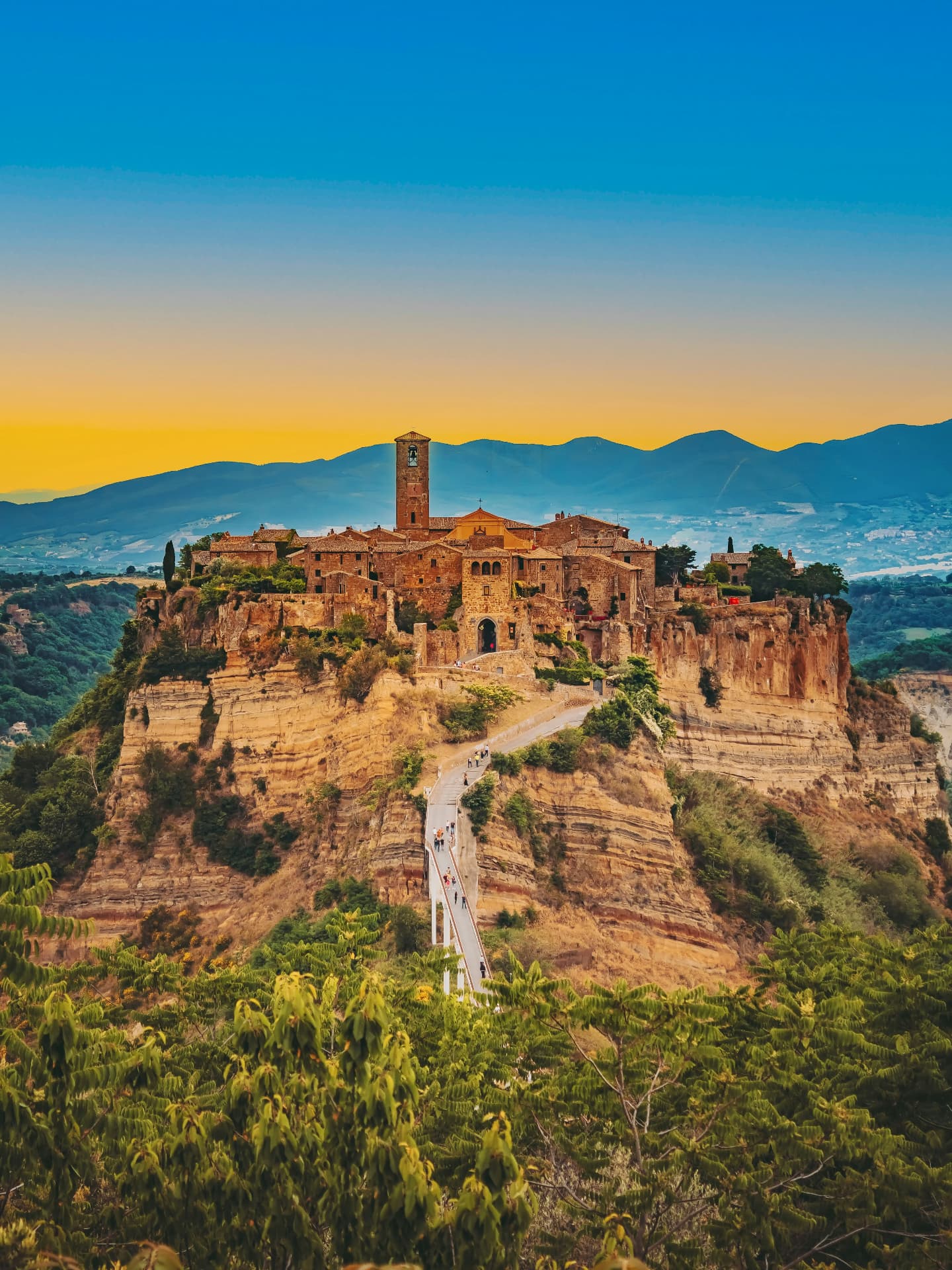 Civita seen from across the valley in the last light, the footbridge reaching toward the gate