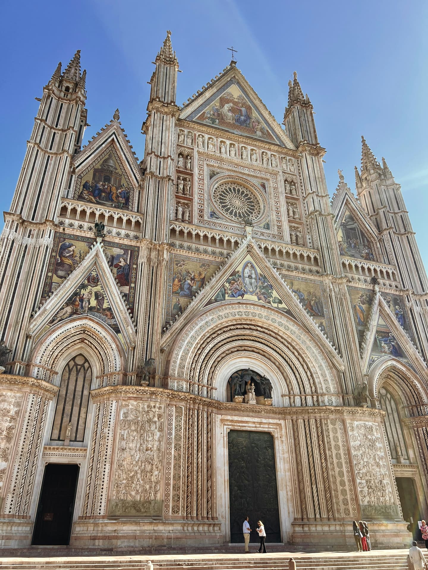 The full gothic façade of Orvieto cathedral, its gold mosaics and rose window above the steps