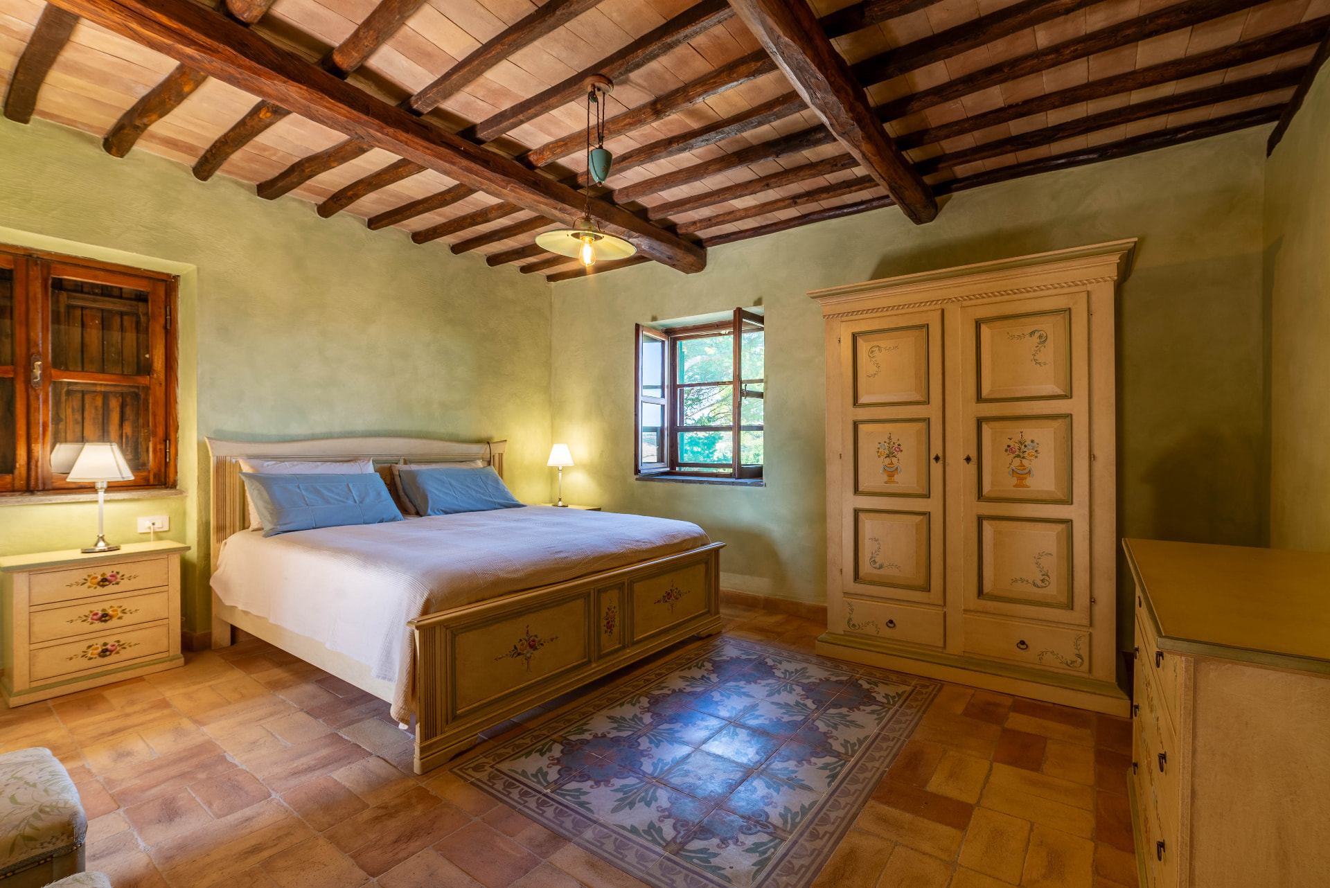The acacia bedroom: painted bed and wardrobe under dark chestnut beams, with its cement-tile carpet