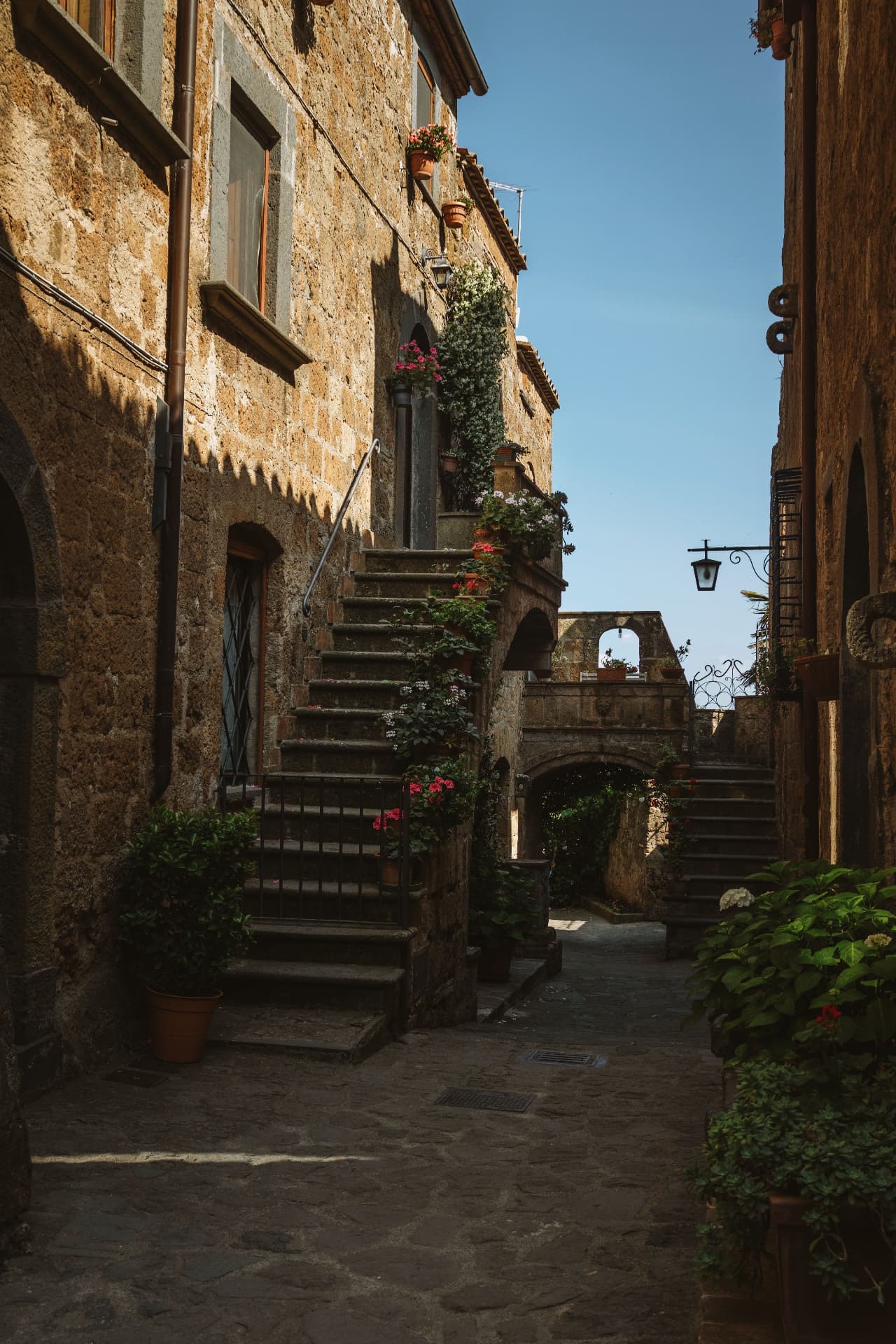 An empty alley in Civita, a stone staircase lined with flowerpots and a lantern on the wall
