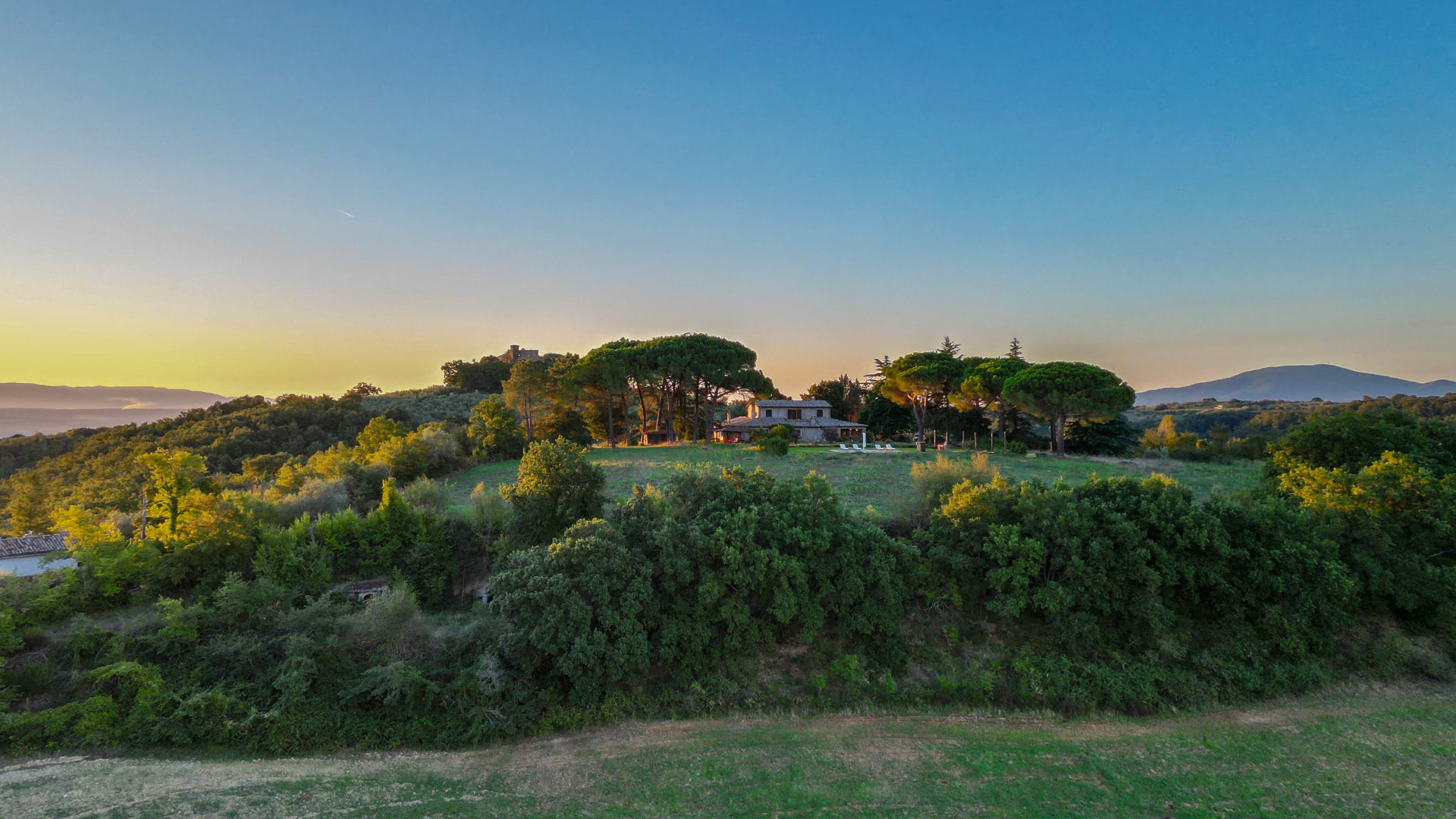 Il Casone on its hilltop, seen from the drone among umbrella pines, olive groves and the valley beyond