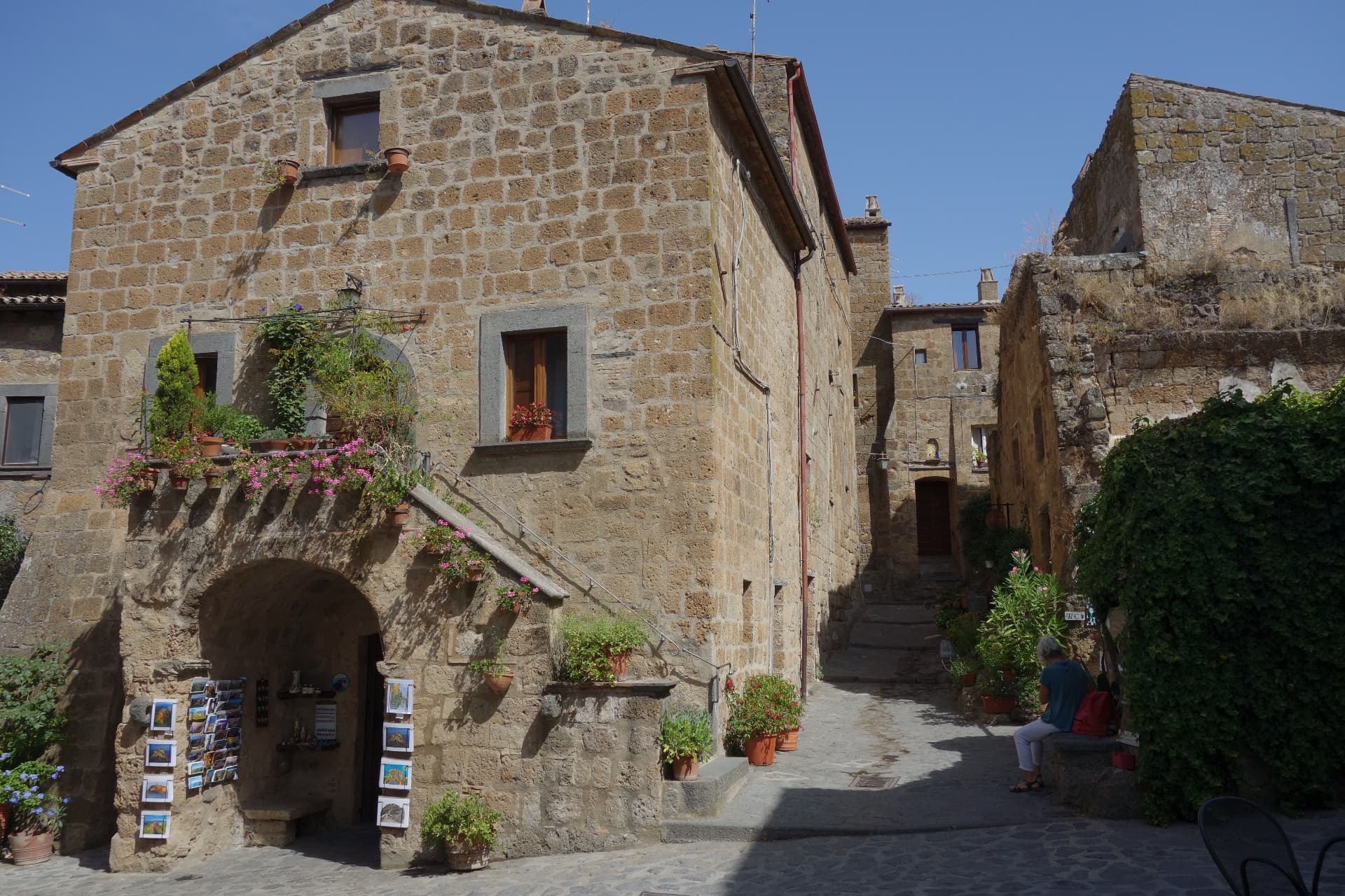A quiet square in Civita in the morning, a postcard stand under an arch and pots of flowers on the steps