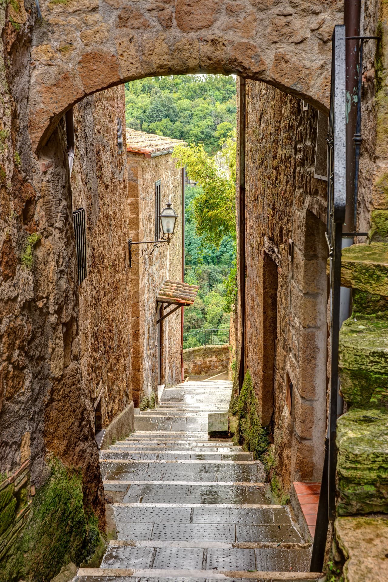 A stepped stone alley under an arch in Pitigliano, a lantern and green valley beyond