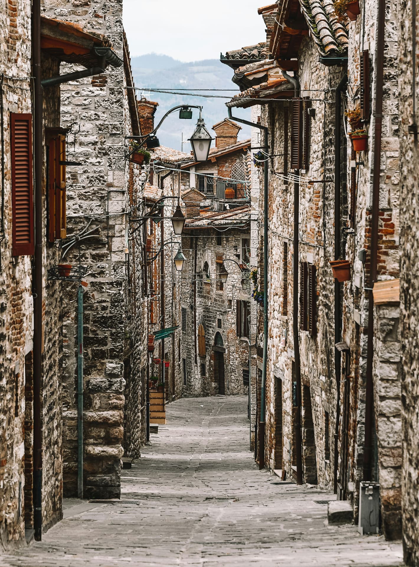 A steep alley of grey stone and hanging lanterns in Gubbio