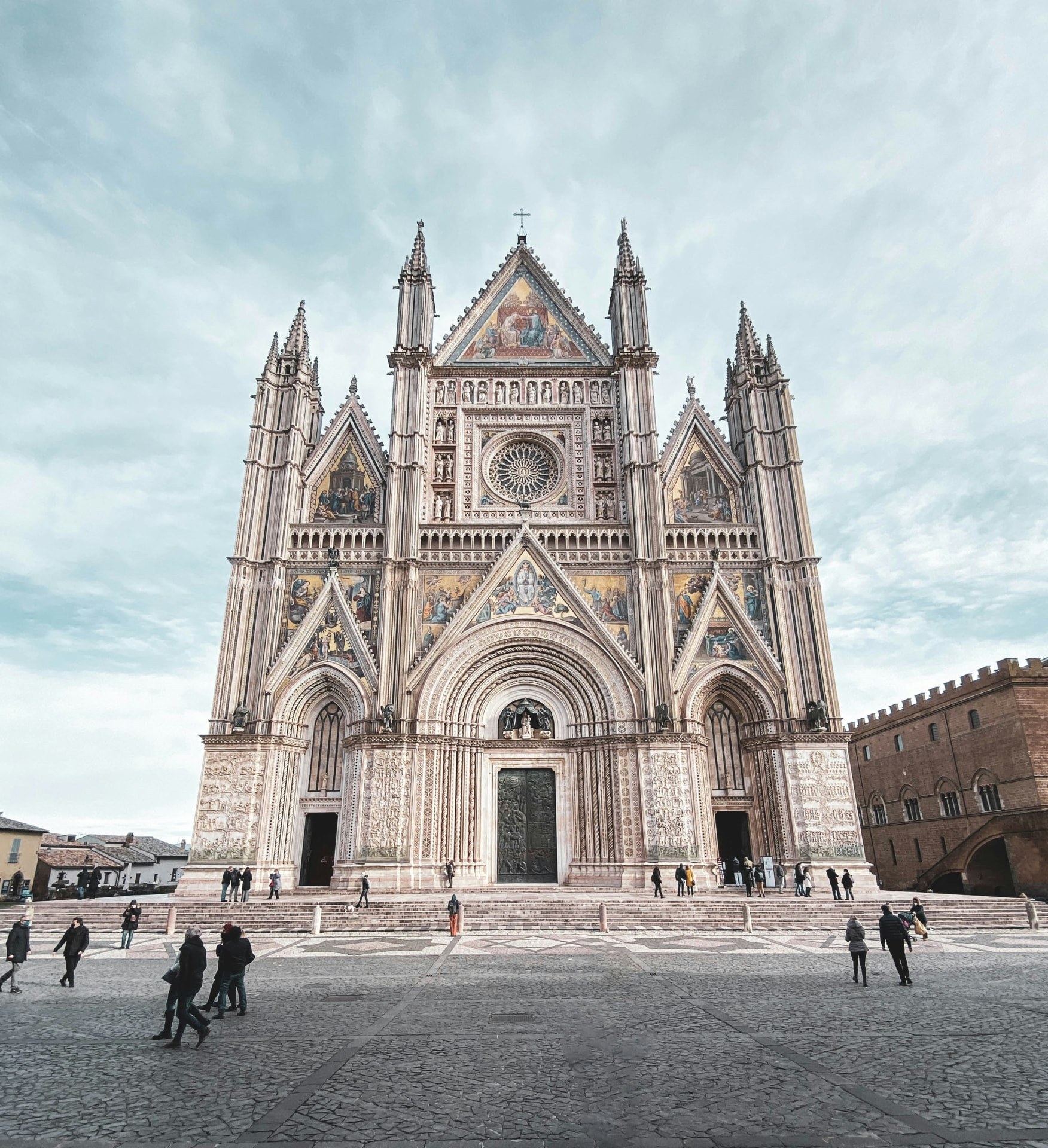 The whole façade of Orvieto cathedral from across the piazza, its rose window and golden mosaics under a pale sky