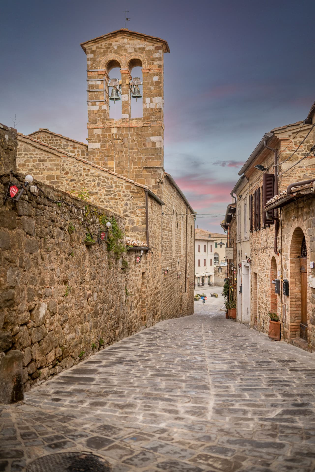 A cobbled lane climbing past a stone bell tower in an Orcia hill town