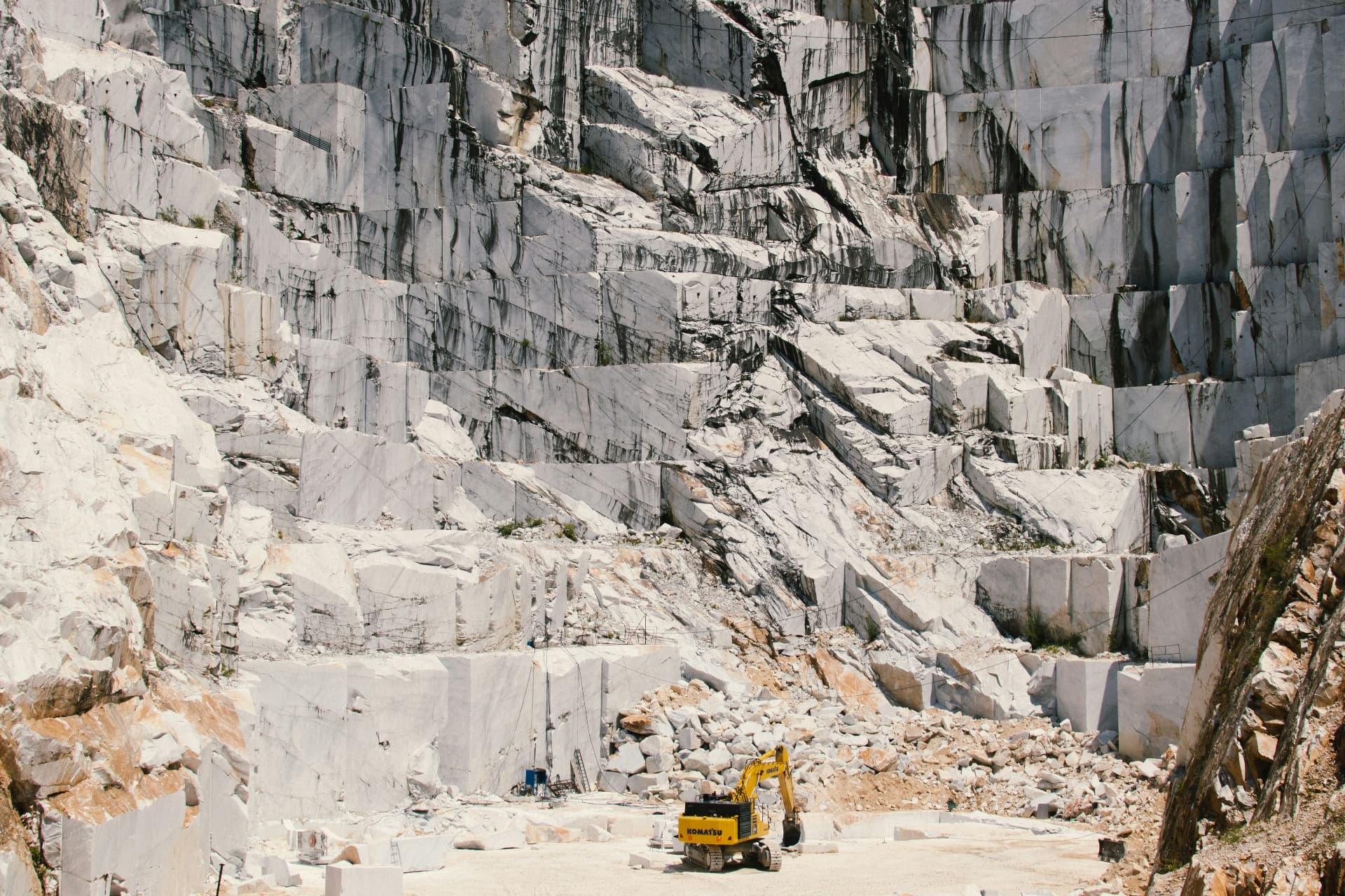 Terraced walls of white marble in the quarry, an excavator at work below