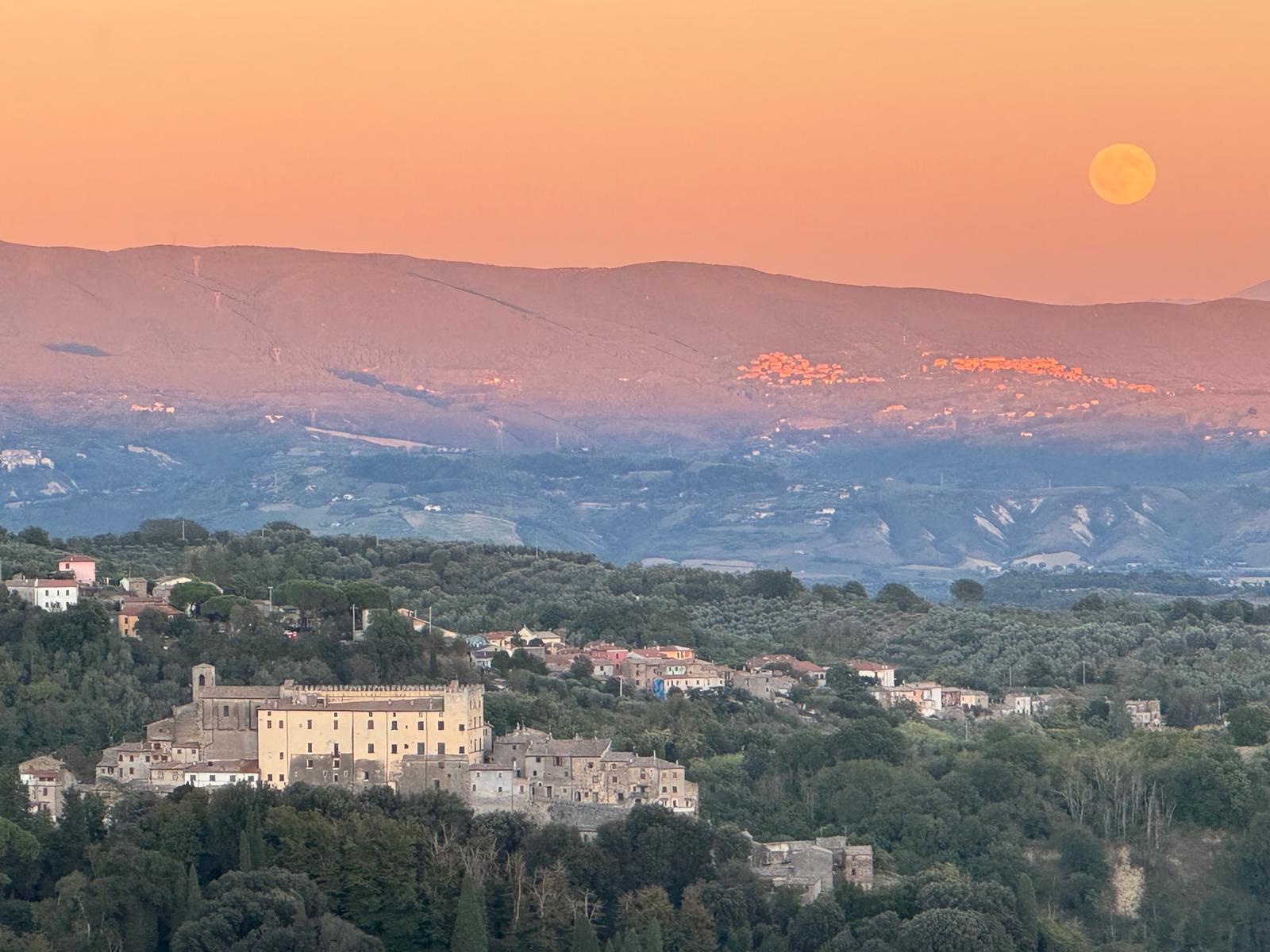 A stone village and its castle on a wooded ridge at dusk