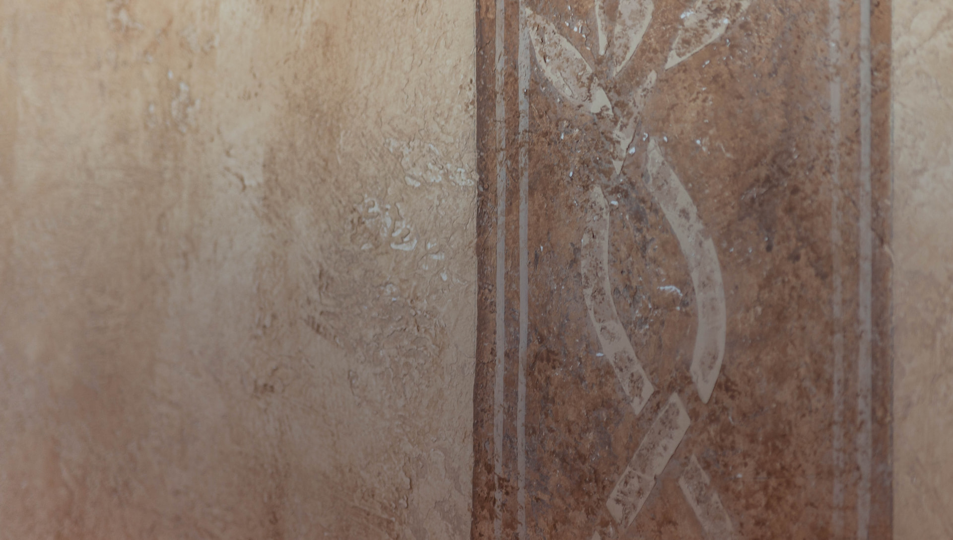 Hand-painted terracotta band with a vine motif on the plastered walls of Il Casone