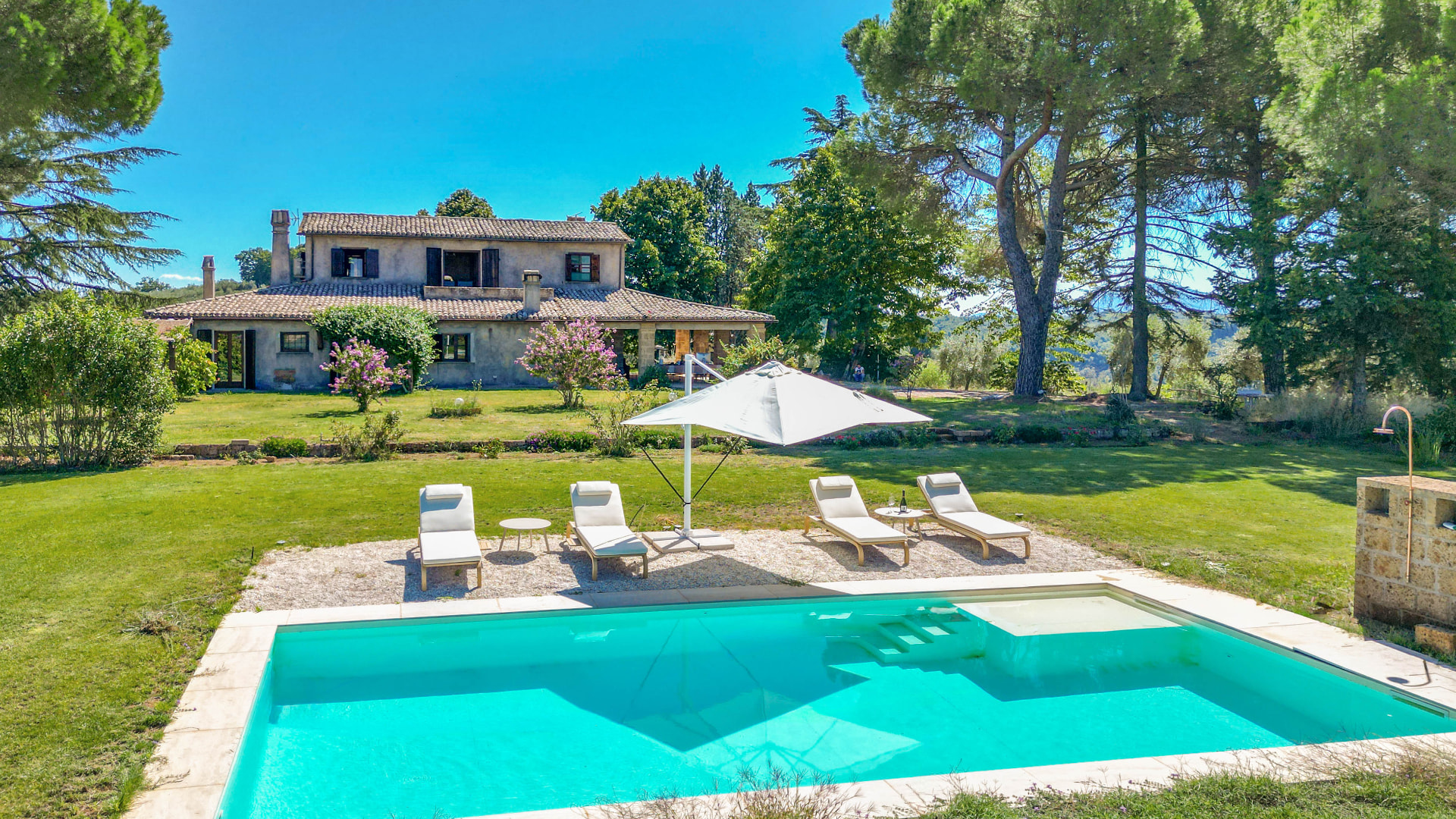 Il Casone and its garden pool with sun loungers and a white umbrella, seen from the drone